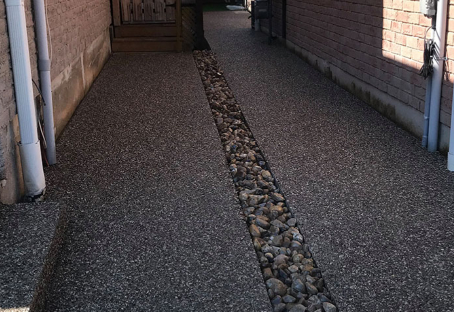 Aggregate side walkway between two homes with a river rock drainage channel