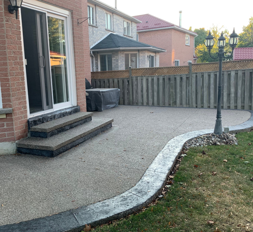 Curved exposed aggregate backyard patio with stamped charcoal border and steps