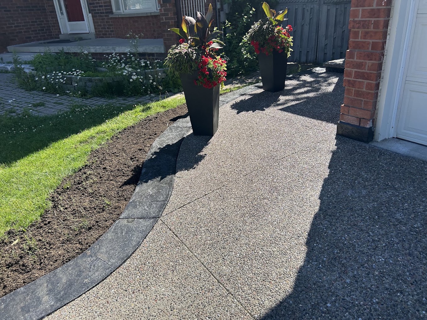 Exposed aggregate walkway curving toward a garage with stamped stone curb